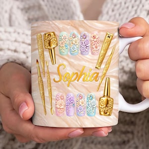 Könnte beinhalten: Weißer Keramikbecher mit marmoriertem Hintergrund und goldenen Nagelwerkzeugen. Der Becher zeigt florale Nageldesigns in Pastellfarben und den Namen "Sophia" in goldener Schrift, sowie eine goldene Nagellackflasche.