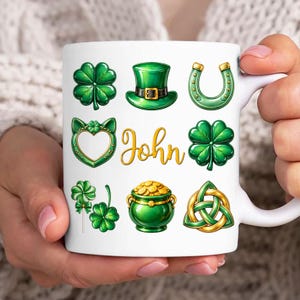 May include: White ceramic mug featuring St. Patrick's Day themed designs. The mug includes green shamrocks, a leprechaun hat, a horseshoe, and a pot of gold. The name "John" is written in gold script. A festive gift.
