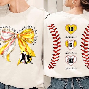 Könnte beinhalten: Cremefarbenes Baseball-Sweatshirt. Die Vorderseite zeigt eine gelb-weiße Schleife mit Baseball-Design und dem Text "Mom of Both". Die Rückseite hat Baseball-Nähte und drei herzförmige Basebälle mit Zahlen und "Name here."