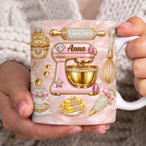 Op de afbeelding: Witte keramische mok met een roze en gouden bakthema. Het ontwerp omvat een roze keukenmixer, deegroller, garde, cupcake en andere bakgereedschappen. De naam "Anna" wordt weergegeven op de mixer.