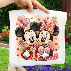 May include: White tote bag featuring Mickey and Minnie Mouse. Mickey holds a rose, and Minnie holds a heart-shaped object with the word "LOVE." The design includes hearts, balloons, and a cupid illustration.