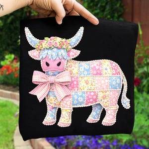 Może przedstawiać: Czarny kwadrat z dekoracyjnym wzorem krowy. Krowa ma różową twarz, kwiatową koronę i dużą różową kokardę. Ciało wykonane jest z pastelowych kwiatowych kwadratów, a rogi są jasnoniebieskie. Projekt przypomina patchwork.