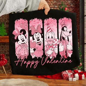 May include: Black fabric featuring Mickey Mouse, Minnie Mouse, Donald Duck, and Goofy in pink Valentine's Day attire. The words "Happy Valentine" are written in pink script below the characters. The design is set against a pink and black background.