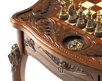 Peut inclure: Table de jeu d'échecs et de backgammon en bois sculpté, avec une finition marron foncé. Les pièces d'échecs sont dorées et argentées, disposées sur un échiquier. La table comprend un tiroir avec une clé et une tête de lion décorative.