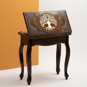 May include: A wooden table with a hinged top featuring a carved tree of life design. The table has four legs with a curved design and a dark brown finish.