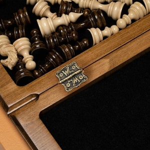 May include: A wooden chessboard with a brass hinge. The board is open and the chess pieces are visible. The pieces are made of wood and are painted in black and white.