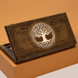 Könnte beinhalten: Eine Holzkiste mit einem keltischen Knotendesign, das einen Lebensbaum zeigt. Die Kiste ist geschlossen und hat eine dunkelbraune Oberfläche.