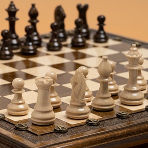 May include: A wooden chessboard with a light brown and dark brown pattern. The board is set up with white and brown chess pieces. The pieces are arranged in a traditional chess starting position. The board is on a wooden table.
