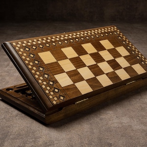 May include: A wooden backgammon set with a checkerboard design. The board features dark and light wood squares, with decorative diamond patterns around the edges. The set is open, showing the playing surface and storage compartments.