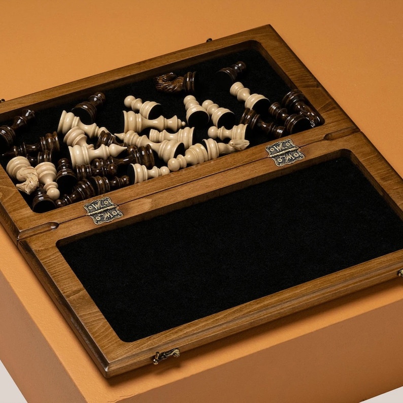 May include: A wooden chessboard with a black felt interior and a set of white chess pieces. The chessboard is closed and the pieces are arranged on the top half of the board.