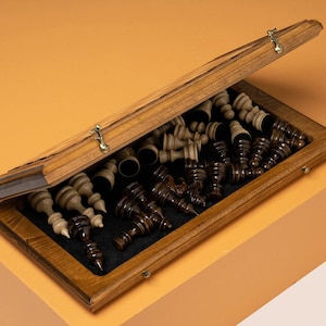 May include: A wooden chess set with a hinged box. The box is open and the chess pieces are visible. The pieces are made of dark wood and light wood. The box is lined with a black felt material.