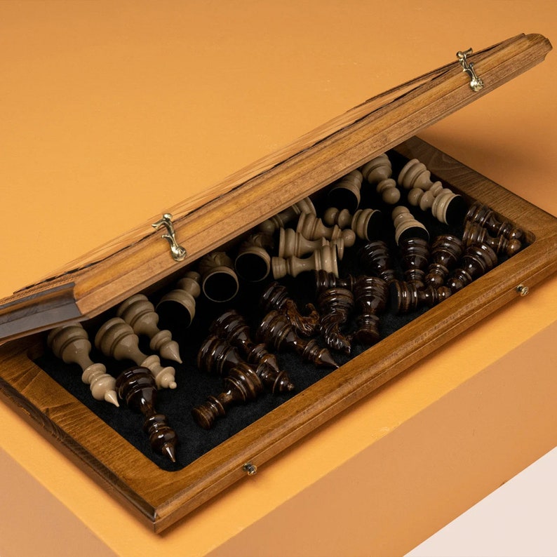 May include: A wooden chess set with a hinged box. The box is open and the chess pieces are visible. The pieces are made of dark wood and light wood. The box is lined with a black felt material.