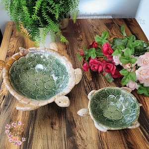May include: Two ceramic turtle bowls with green and brown swirl designs. The larger bowl is on the left and the smaller bowl is on the right. Both bowls are on a wooden surface.