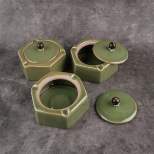May include: Three green ceramic hexagonal ashtrays with lids. Each lid has a small black knob on top.