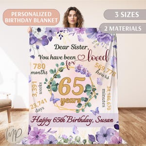 May include: A pink and purple floral birthday blanket with a gold frame and the text "Dear Sister, You have been loved for 65 years. Happy 65th Birthday, Susan".