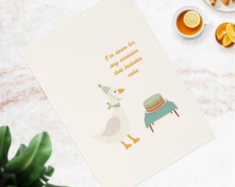 Könnte beinhalten: Cremefarbenes Küchentuch mit einer skurrilen Illustration einer Gans mit Partyhut und Kuchen. Der Text lautet: „Ich bin für jeden Anlass zu haben, der Kuchen beinhaltet.“ Ein lustiger, dekorativer Artikel für die Küche.