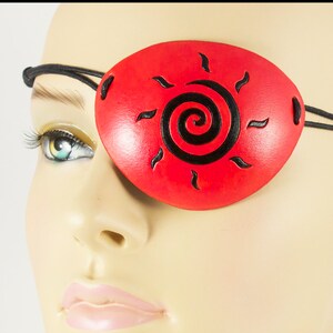 May include: Red leather eye patch with a black spiral sun design.
