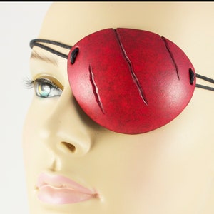 Peut inclure: Un cache-œil en cuir rouge avec un aspect vieilli et des coutures noires. Le cache-œil est porté sur l'œil droit d'un mannequin.