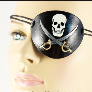 Handmade leather eyepatch with a Jolly Roger skull-and-crossed-swords design carved and painted on the leather. The skull is bone-white on black, and the swords are painted silver with golden hilts.