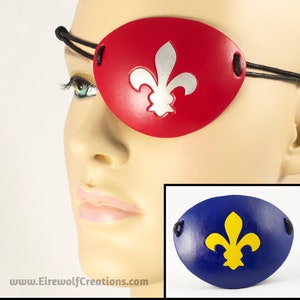 May include: A red leather eye patch with a silver fleur-de-lis design. A blue leather eye patch with a yellow fleur-de-lis design is shown below.