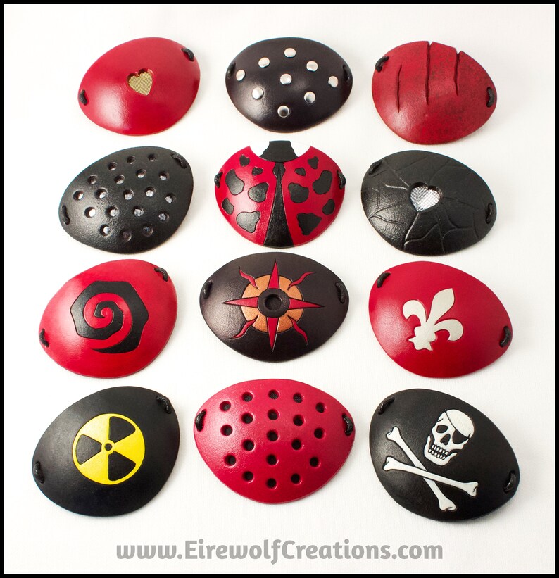 An assortment of handmade leather eye patches with various designs, including rivets, scarred, ladybug, spiral, fleur de lis, radiation hazard, Jolly Roger, see-through hearts, see-through perforated, and see-through compass rose.