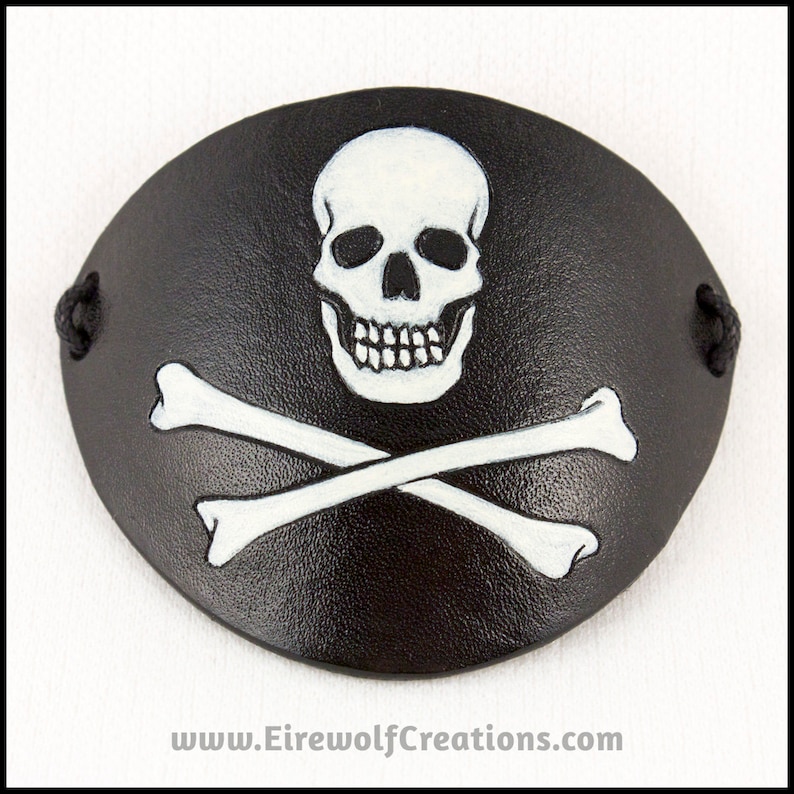 Handmade leather eyepatch with a skull-and-bones Jolly Roger carved into the leather and painted bone-white on a black background.