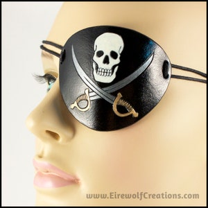 Handmade leather eyepatch with a Jolly Roger skull-and-crossed-swords design carved and painted on the leather. The skull is bone-white on black, and the swords are painted silver with golden hilts.