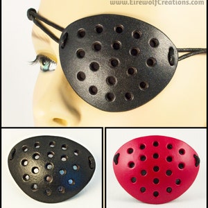 Könnte beinhalten: Zwei Augenklappen, eine schwarze und eine rote, mit einem perforierten Design. Beide Klappen haben ein elastisches Band.