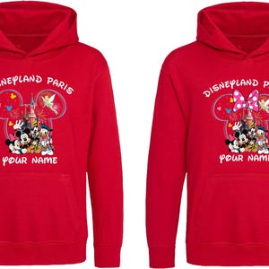 May include: Red hooded sweatshirts with "Disneyland Paris" printed above a graphic of Mickey Mouse, Minnie Mouse, Donald Duck, and Goofy. The text "Your Name" is below the graphic. One sweatshirt has a bow.