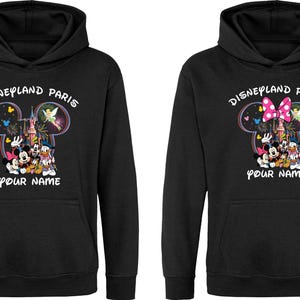 May include: Black hooded sweatshirt featuring a Disneyland Paris design. The design includes Mickey Mouse, Minnie Mouse, Donald Duck, and other characters. The text "Disneyland Paris" and "Your Name" are also visible.