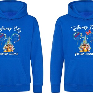 May include: Two blue hoodies with a Disney Trip design. The design includes the text "Disney Trip" above a castle and Disney characters. Below the design is the text "YOUR NAME". One hoodie has a red bow.