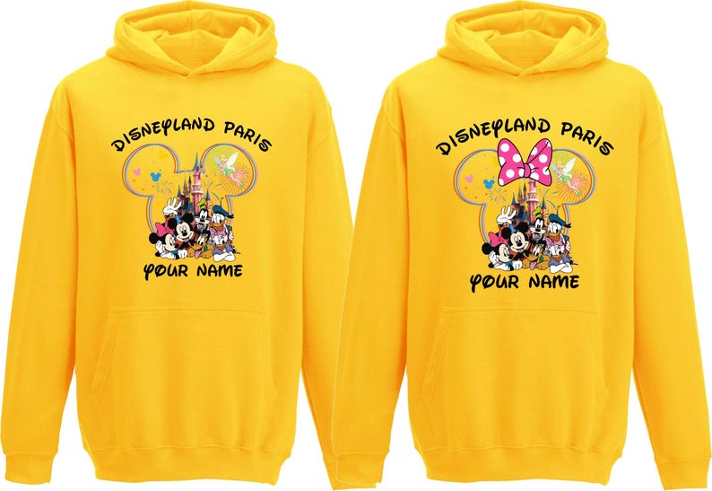 May include: Two yellow hoodies with the text "Disneyland Paris" and a graphic of Disney characters. One hoodie has a pink bow, the other has a Mickey Mouse head design. The text "Your Name" is below the graphic.