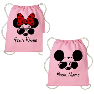 May include: Two pink drawstring bags with a Mickey Mouse and Minnie Mouse design. The bags have black sunglasses and the text "Your Name" printed on them.