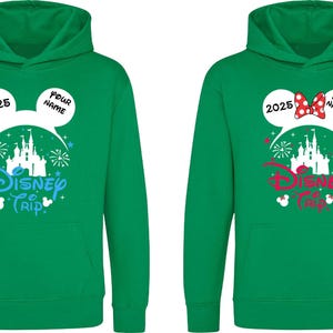 K&ouml;nnte beinhalten: Zwei gr&uuml;ne Kapuzenpullover mit einem Disney Trip-Design. Einer hat ein blaues Design, der andere ein rotes Design. Beide haben Mickey Mouse-Ohren mit dem Jahr 2025 und Platz f&uuml;r einen Namen. Das Design beinhaltet ein Schloss und Feuerwerk.