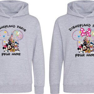 May include: Two light gray hoodies with a Disneyland Paris graphic. The graphic includes Mickey Mouse, Minnie Mouse, Donald Duck, and other Disney characters. The text "Disneyland Paris" and "Your Name" are also printed on the hoodies.