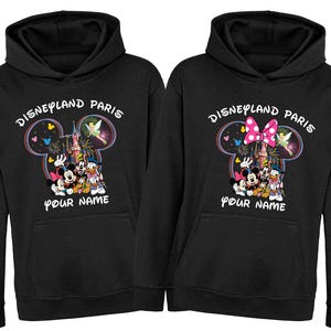 May include: Two black hoodies with a Disneyland Paris graphic. The graphic features Mickey and Minnie Mouse, Donald Duck, and Goofy, with the text "Disneyland Paris" and "Your Name". The design includes a castle and fireworks.
