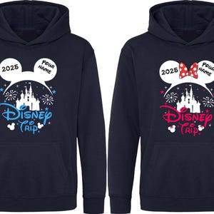K&ouml;nnte beinhalten: Marineblaue Kapuzenpullover mit einem Disney Trip-Design. Einer hat ein blaues Design, der andere ein rosa Design mit einer roten Schleife. Beide haben eine Schlossgrafik, das Jahr 2025 und Platz f&uuml;r einen Namen.