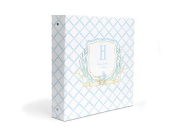 May include: A white three-ring binder featuring a light blue diamond lattice pattern. The center displays a crest with the letter H, the text Henry Lewis, and the date 1.5.2023, surrounded by green laurel branches and a yellow ribbon accent.