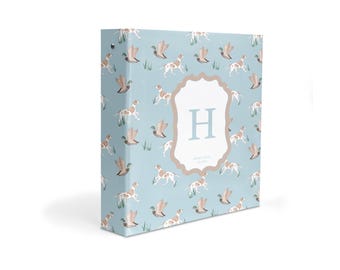 May include: A light blue three-ring binder featuring a repeating pattern of brown and white hunting dogs and ducks in grass. A central white scalloped label displays a large light blue letter H above the text Henry Louis 1.05.2024.