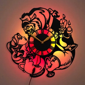 May include: A black silhouette wall clock featuring characters from the Disney movie Beauty and the Beast. The clock face is red and yellow with black Roman numeral markings. The characters include Belle, Beast, Lumiere, and Cogsworth.