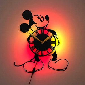 May include: A black silhouette of Mickey Mouse holding a clock with Roman numerals. The clock face is black with gold hands and a red and yellow glow behind it.
