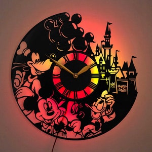 May include: A black vinyl record clock featuring Mickey Mouse, Donald Duck, Goofy, and a silhouette of Cinderella's castle. The clock face is illuminated with a red, orange, and yellow gradient.