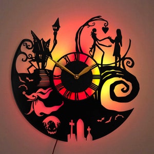 Puede incluir: Un reloj de pared de silueta negra con una función de brillo en la oscuridad. El reloj presenta un diseño de Jack Skellington y Sally de la película Pesadilla antes de Navidad. El reloj tiene un fondo negro con un efecto de brillo en la oscuridad rojo, naranja y amarillo.