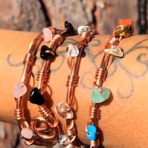 May include: Three wire-wrapped bracelets made of copper-toned metal. Each bracelet features small, irregular, polished gemstone chips in various colors, including pink, black, clear, green, blue, and orange, secured within the twisted metal wire.