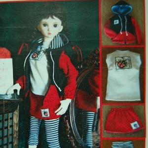 May include: A doll wearing a red and black hooded jacket, a white shirt with a ladybug graphic, a red skirt with white polka dots, and black and white striped leggings. The doll is standing in front of a mirror.