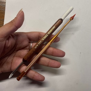 May include: Two Kemper Tools USA A3R clay sculpting tools. One tool has a wooden handle with a white tip and a metal blade. The other tool is gold-colored with a textured handle and a red, pointed tip. Both tools are designed for sculpting.