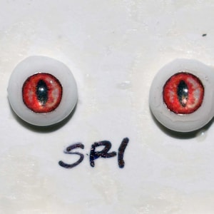 May include: Two red glass eyes with black pupils, set on a white background. The text "SPI" is written below the eyes.