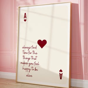 Puede incluir: Una impresión artística enmarcada con el diseño de la carta As de Corazones. La carta crema muestra los símbolos de la baraja y el texto "always find time for the things that makes you feel happy to be alive" en estilo manuscrito.