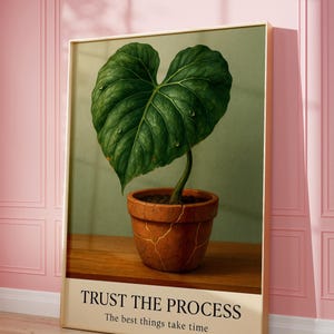 May include: A framed botanical print featuring a large, heart-shaped green leaf with water droplets, emerging from a terracotta pot. The print includes the text "TRUST THE PROCESS" and "The best things take time."