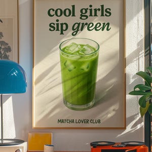 May include: A framed poster with the text "cool girls sip green" and a glass of green matcha drink with ice cubes. The poster is part of a room decor with a record player and other items.